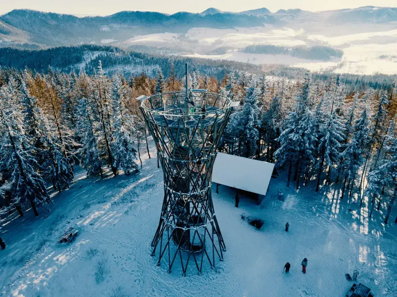 Wieża widokowa na borowej górze w zimowej scenerii. Śnieg pokrywa drzewa i ziemię, tworząc bajkowy krajobraz.
