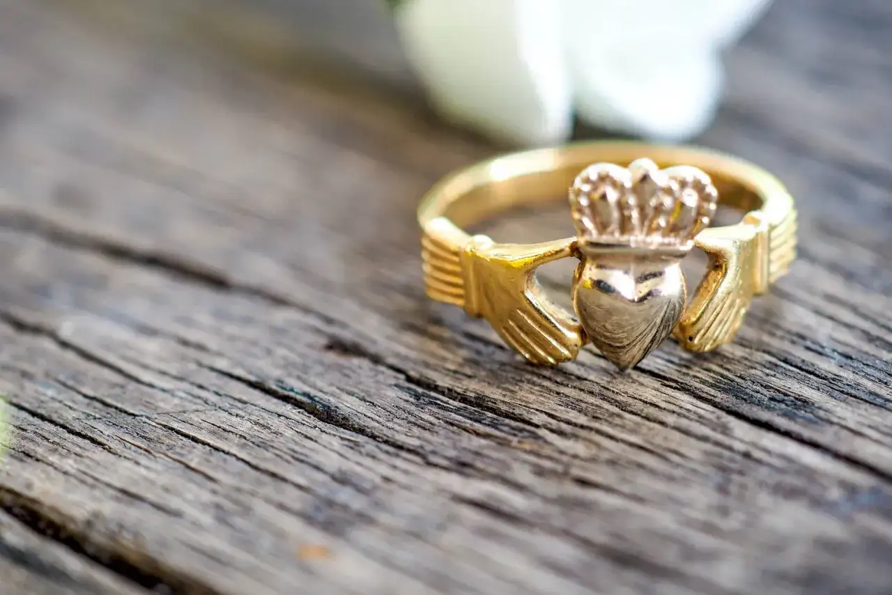 Un anello Claddagh d'oro, simbolo di amore, lealt&agrave; e amicizia, posato su un tavolo di legno grezzo.