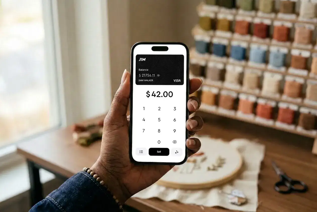 Dłoń trzyma smartfon z włączonym **NFC w telefonie**, wyświetlający aplikację płatniczą z kwotą 42.00$. W tle widać regał z kolorowymi nićmi.