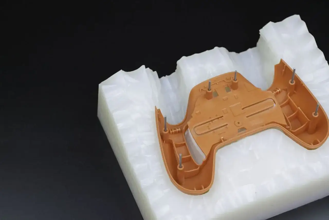 A brown plastic part is placed in a white mold. This is a step in polyurethane vacuum casting, creating a replica of the part.