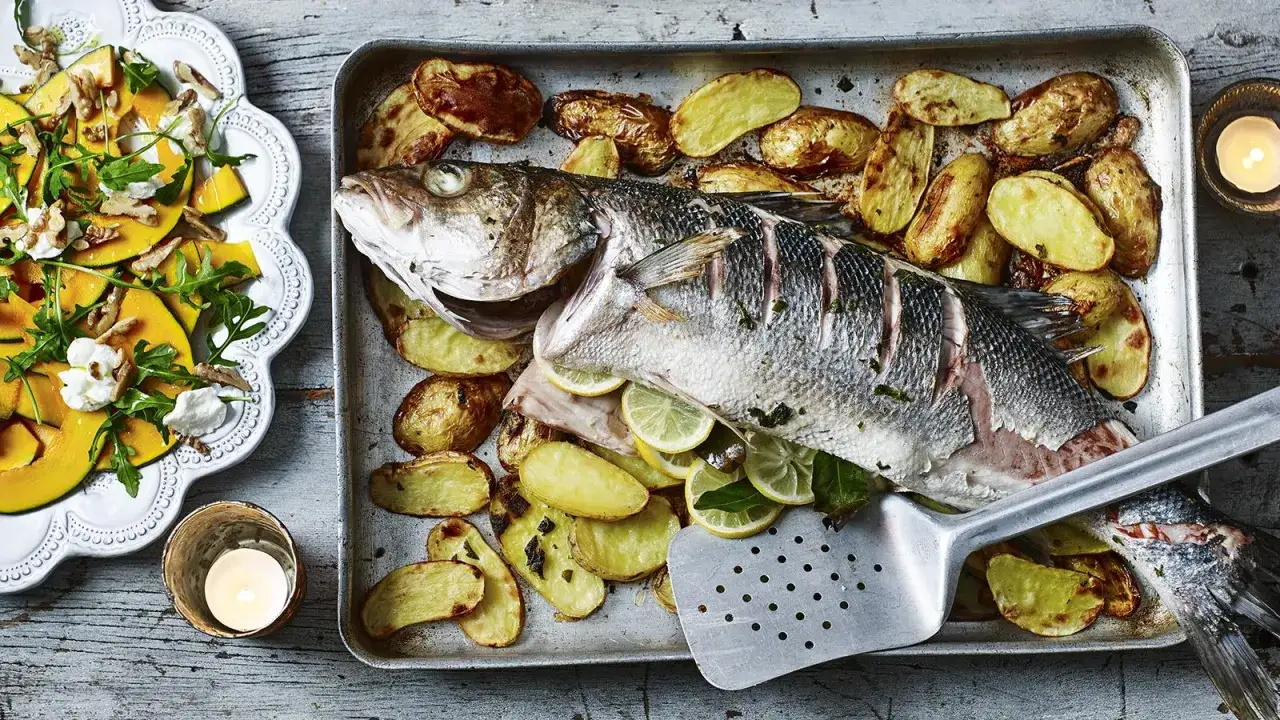 Lubina al horno con patatas asadas y rodajas de lim&oacute;n. Un plato principal perfecto para una cena especial.