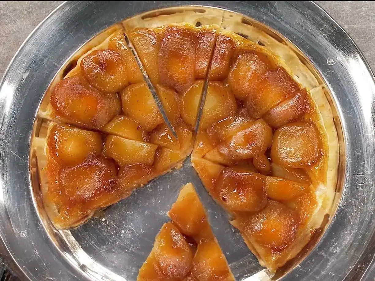En gyllene tarte tatin med karamelliserade &auml;pplen p&aring; ett silverfat, redo att avnjutas.