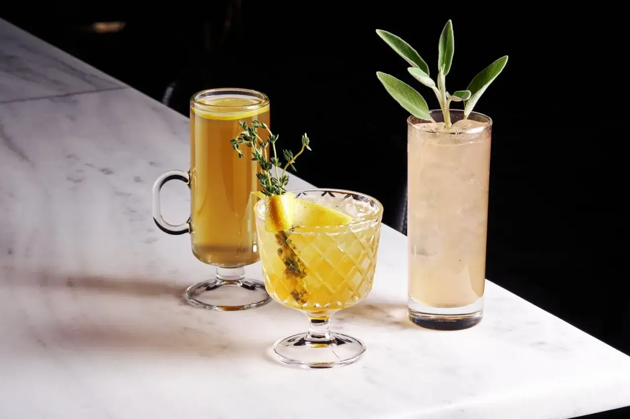 Trois cocktails rafraîchissants, dont un avec du thym et du citron, sont présentés sur un comptoir en marbre.
