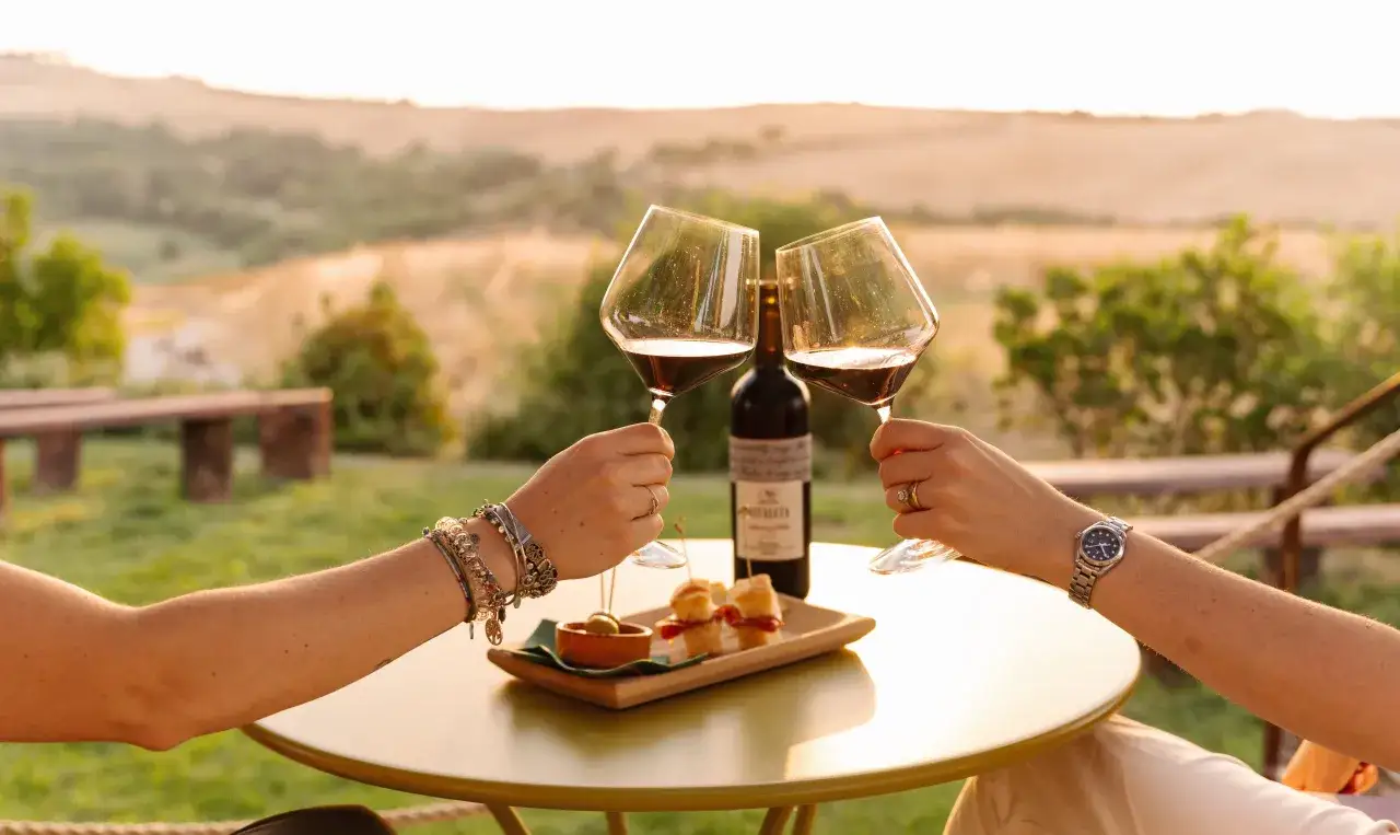 Brindisi al tramonto con vino rosso e stuzzichini, con vista sulle colline toscane vicino a Castel d'Orcia.