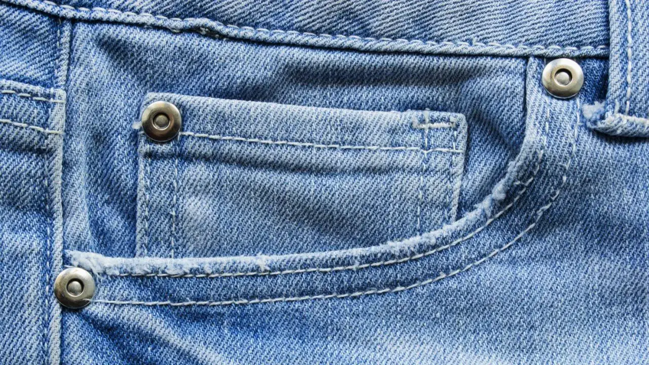 Close-up of blue denim jeans showing stitching and metal rivets on the pocket.