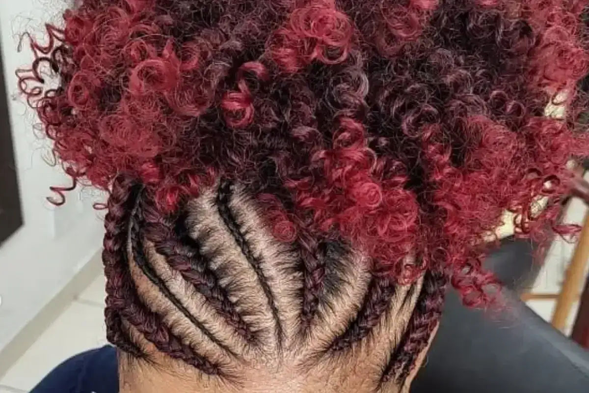 Tresses coll&eacute;es sur le cuir chevelu, contrastant avec des cheveux boucl&eacute;s rouge vif et noir.