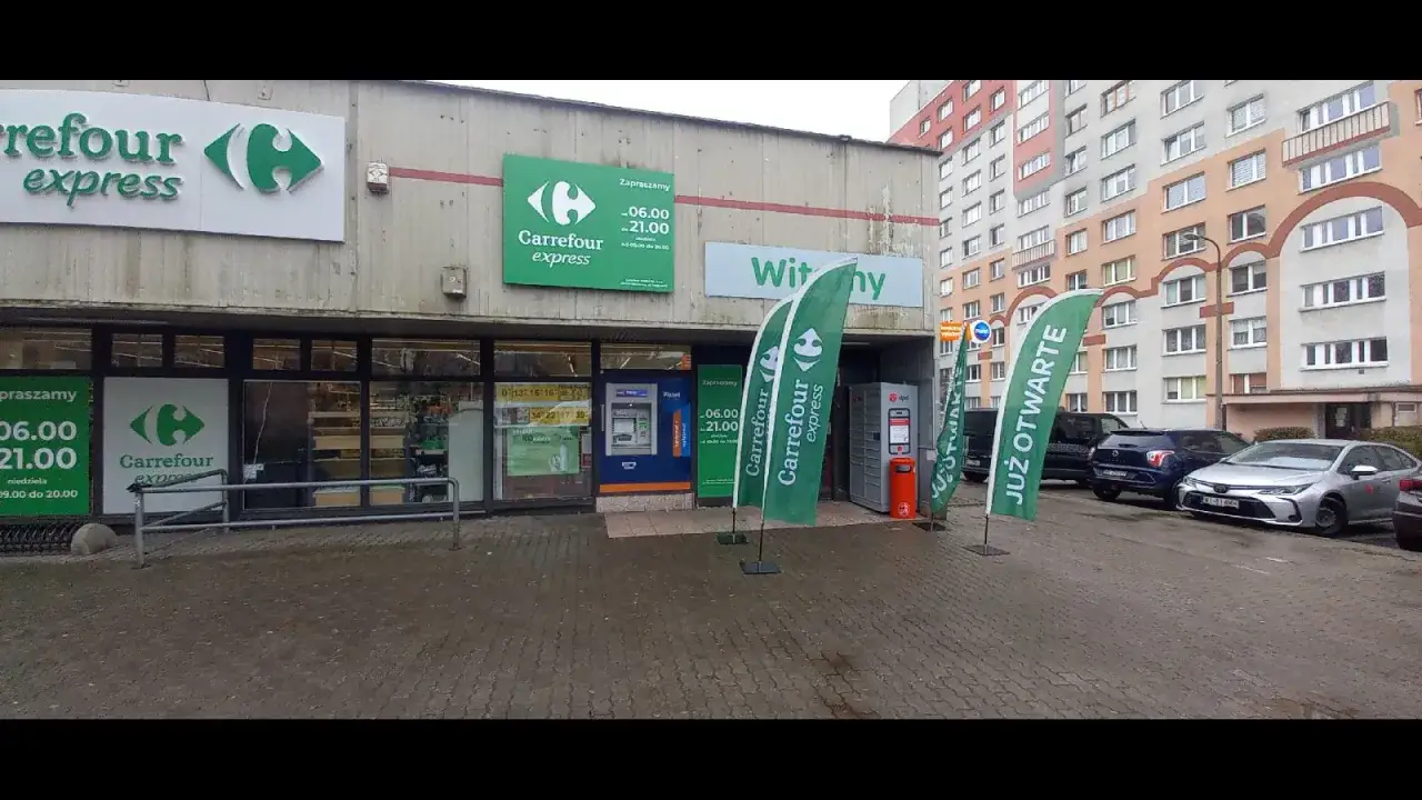 Przed sklepem Carrefour Express stoją zielone flagi z logo. Obok znajduje się paczkomat DPD.