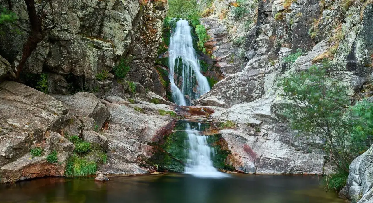 Cascada en la ruta de las cascadas del purgatorio, con agua cayendo entre rocas cubiertas de musgo y vegetaci&oacute;n.