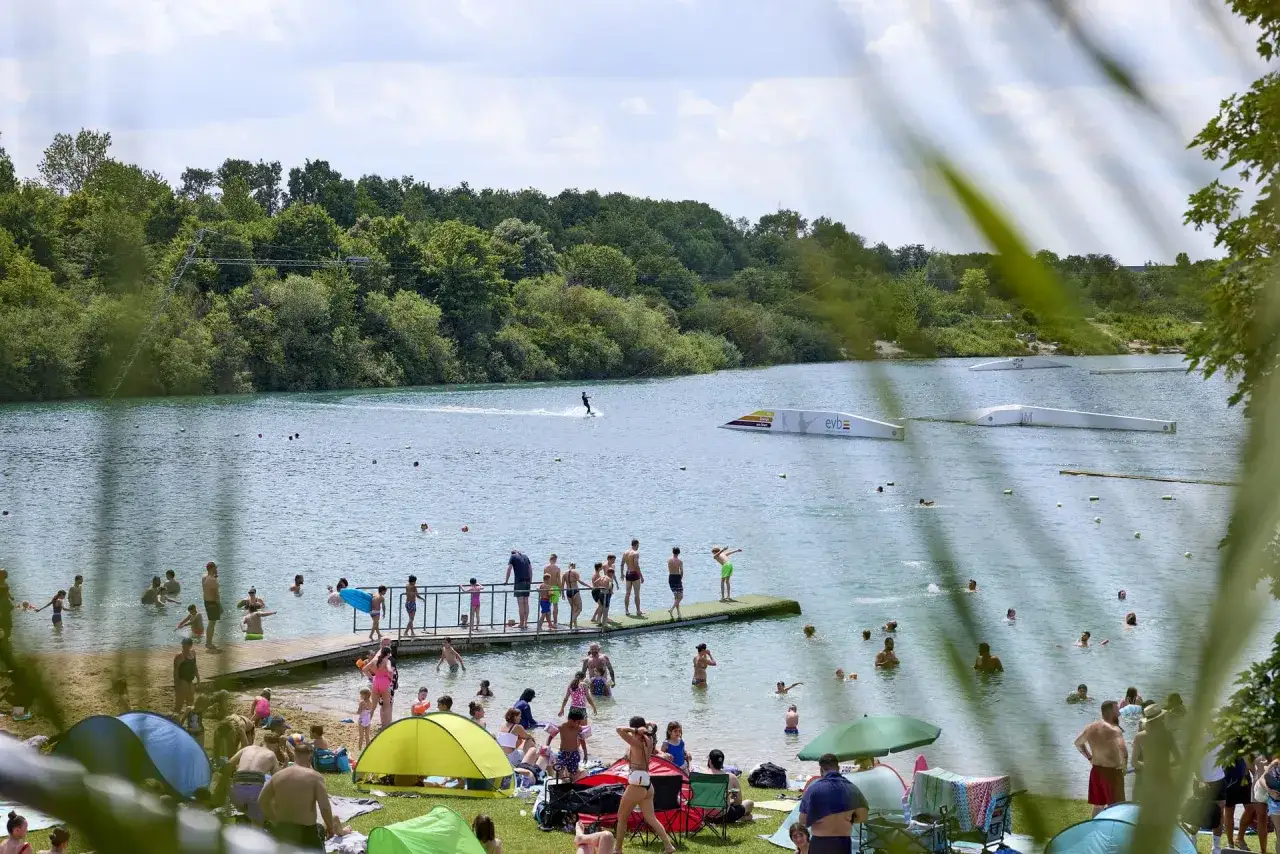 Menschen genießen einen sonnigen Tag am **Beckum See** mit Wasserski und Entspannung am Ufer.