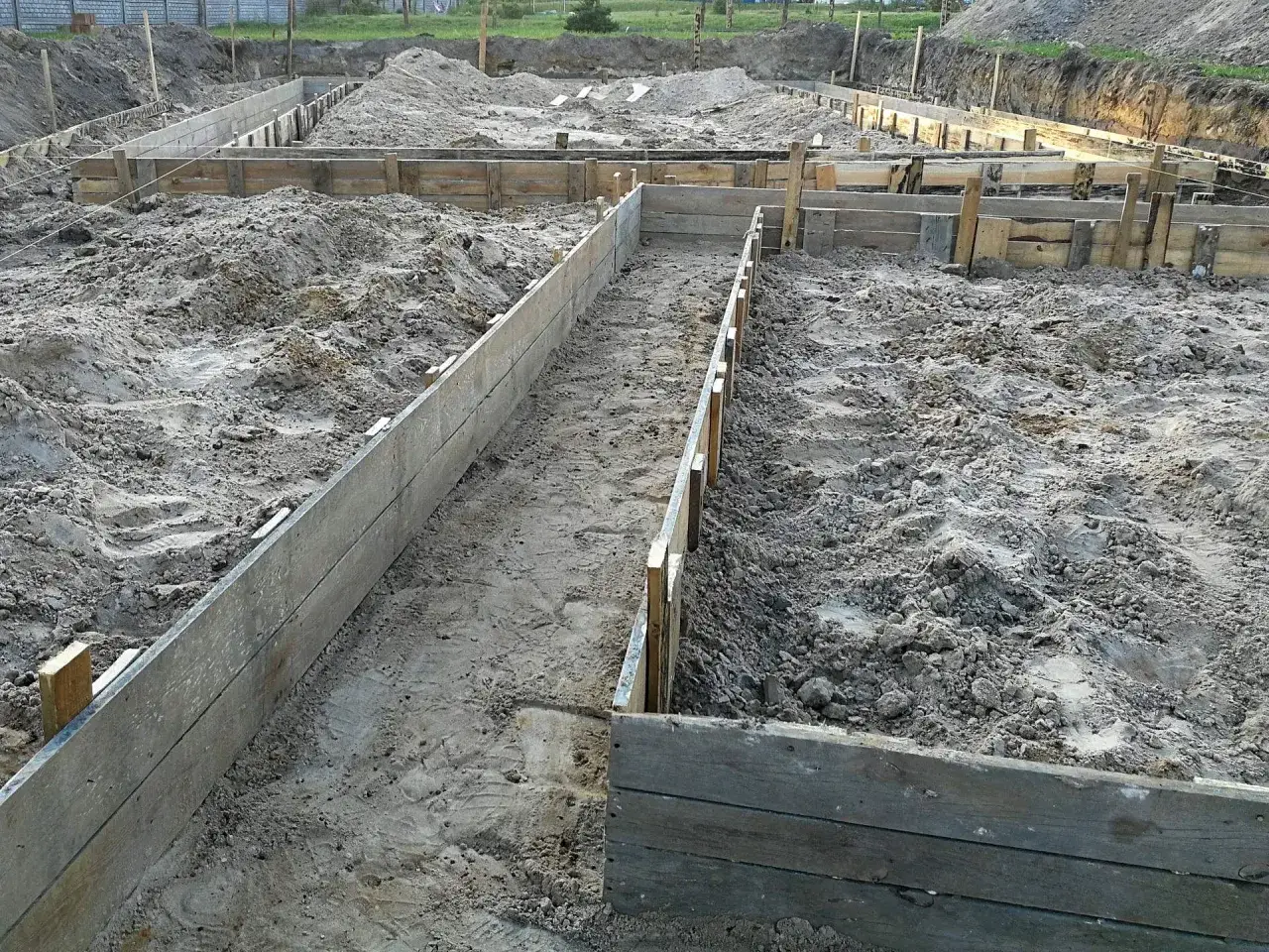 Drewniane szalunki wyznaczają kształt przyszłego fundamentu. Czekają na odpowiedni beton na fundament, który zapewni stabilność budowli.