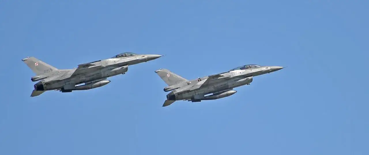 Dwa samoloty wojskowe F-16 w locie, jeden za drugim, na tle błękitnego nieba.