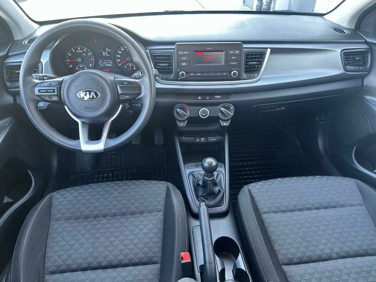 Wnętrze Kia Rio 4: kierownica, deska rozdzielcza z radiem i nawiewami, dźwignia zmiany biegów i fotele.