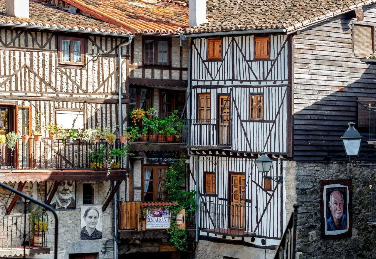 Casas con entramado de madera y balcones floridos en la sierra de Francia. Retratos cuelgan de las fachadas, invitando a descubrir la historia de estos pueblos.