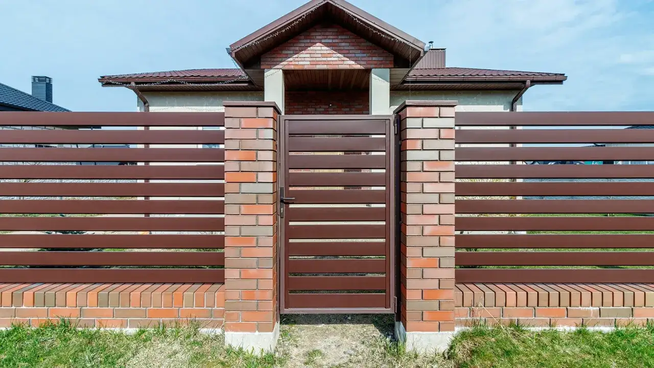 Solidne ogrodzenie z klinkieru i brązowych paneli, z bramą wjazdową.