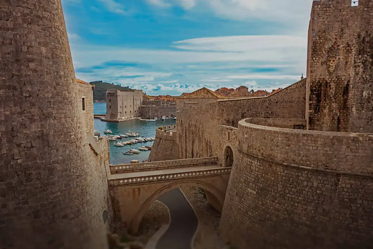 Dubrovniks gamla stadsmurar, där Game of Thrones spelades in, med en hamn full av båtar och en bro över en väg.