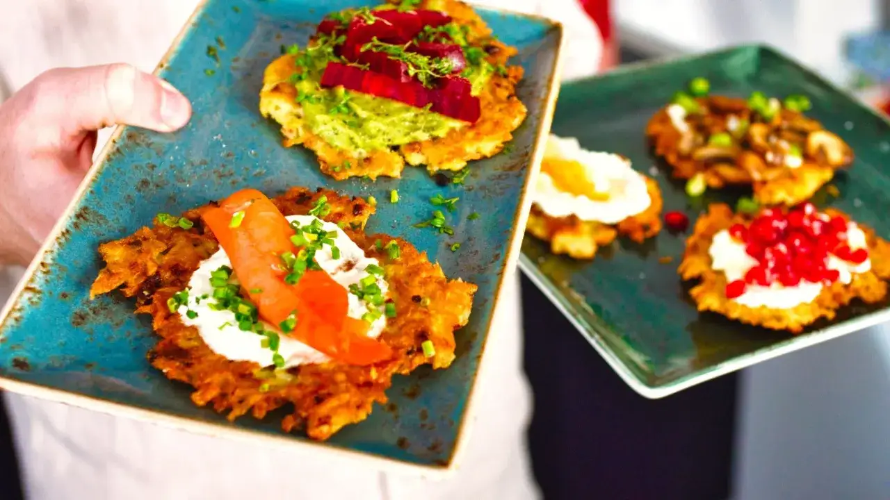Kartoffelpuffer im Backofen, belegt mit Lachs, Rote Bete und Granatapfelkernen, serviert auf blauen und gr&uuml;nen Tellern.