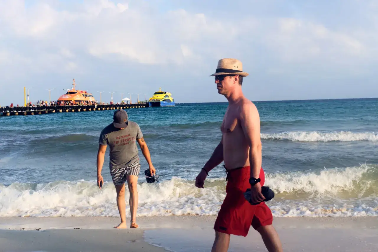 35mm vs 50mm street photography: Two men walk on a beach with ferries docked at a pier in the background.