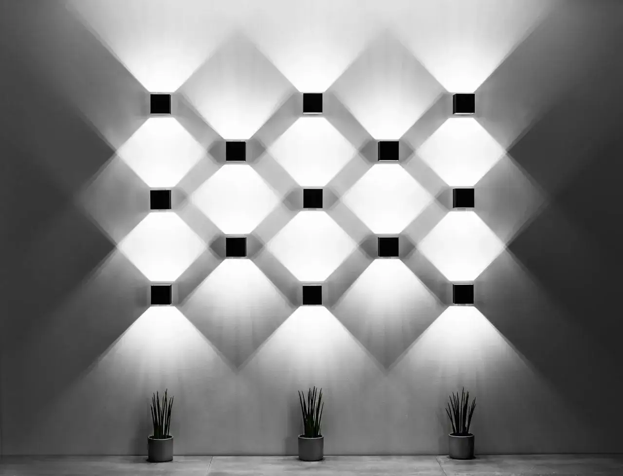 Ściana z rzędem kwadratowych lamp, tworzących geometryczny wzór światła i cienia. Każda lampa kostka rzuca snop światła, tworząc romby na ścianie.