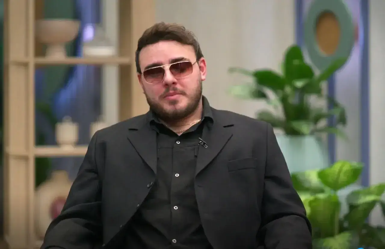 Krystian Ochman w czarnym garniturze i okularach, jakby szykował się na spotkanie z żoną.