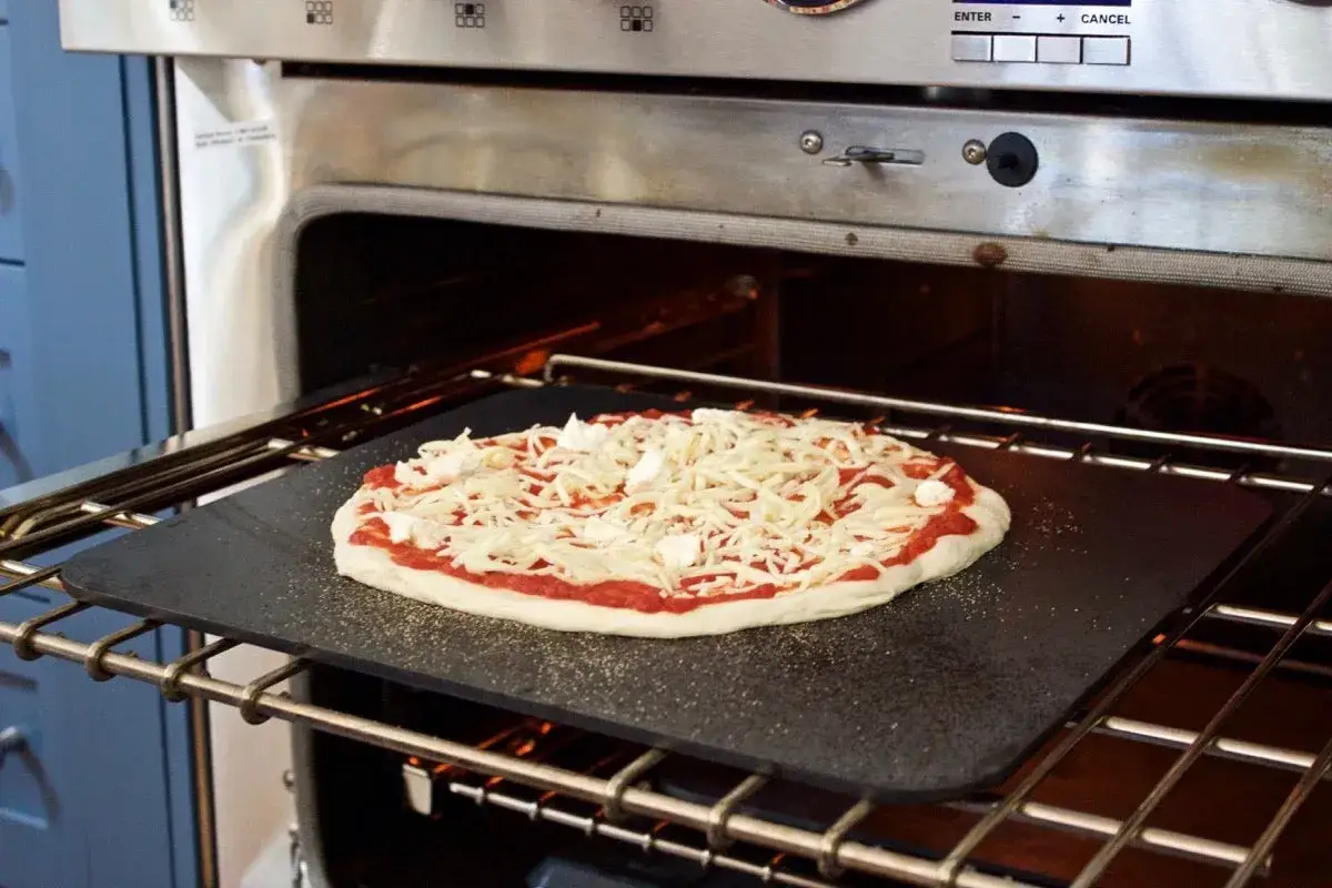 En pizzadeg som på pizzeria, med tomatsås och rikligt med ost, väntar på att gräddas i ugnen på en baksten.