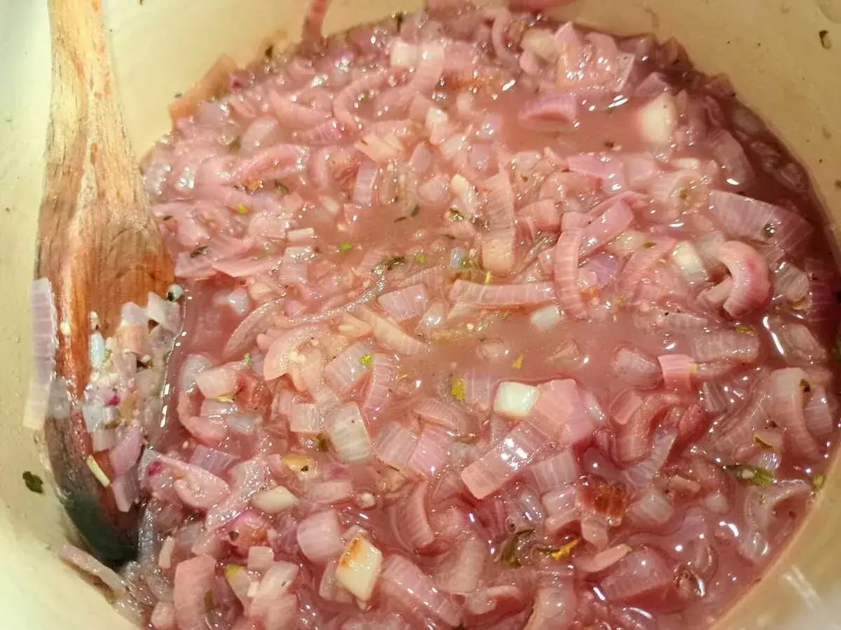 Cuillère en bois remuant des oignons rouges mijotés dans une sauce au vin blanc pour viande.