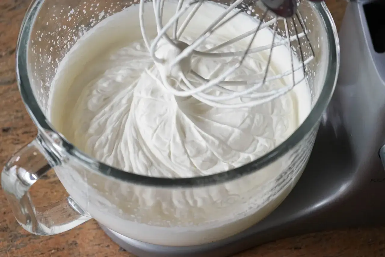 La crème fouettée est presque prête dans le bol en verre. Le batteur est en train de la monter, montrant comment faire de la chantilly parfaite.