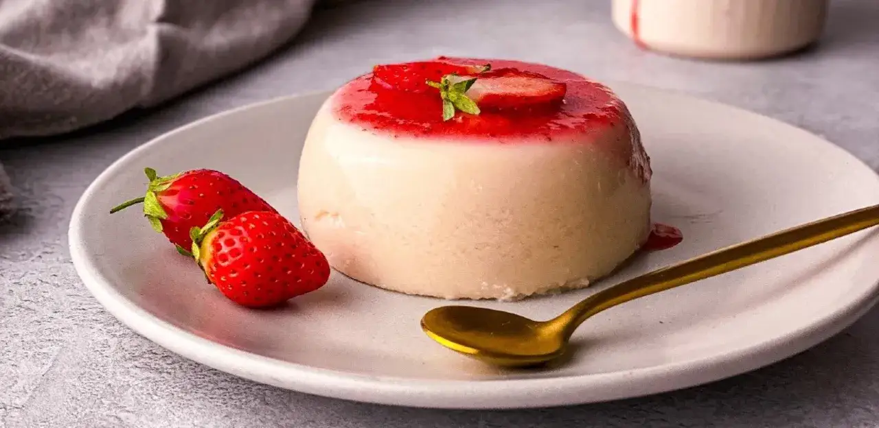 En kr&auml;mig italiensk pannacotta med jordgubbss&aring;s och f&auml;rska jordgubbar, redo att avnjutas med en gyllene sked.