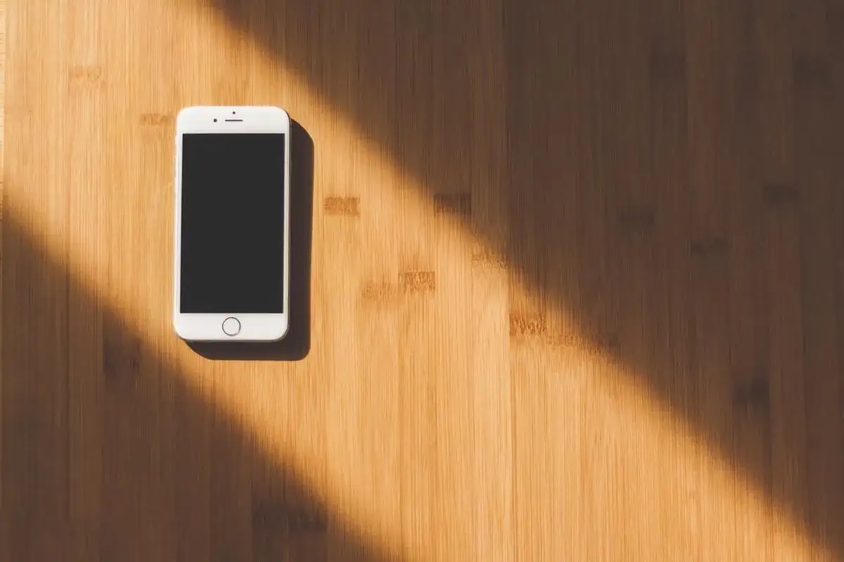 Smartphone bianco su superficie in legno, illuminato da un raggio di sole. Simboleggia il ghosting significato, l'atto di sparire senza spiegazioni.