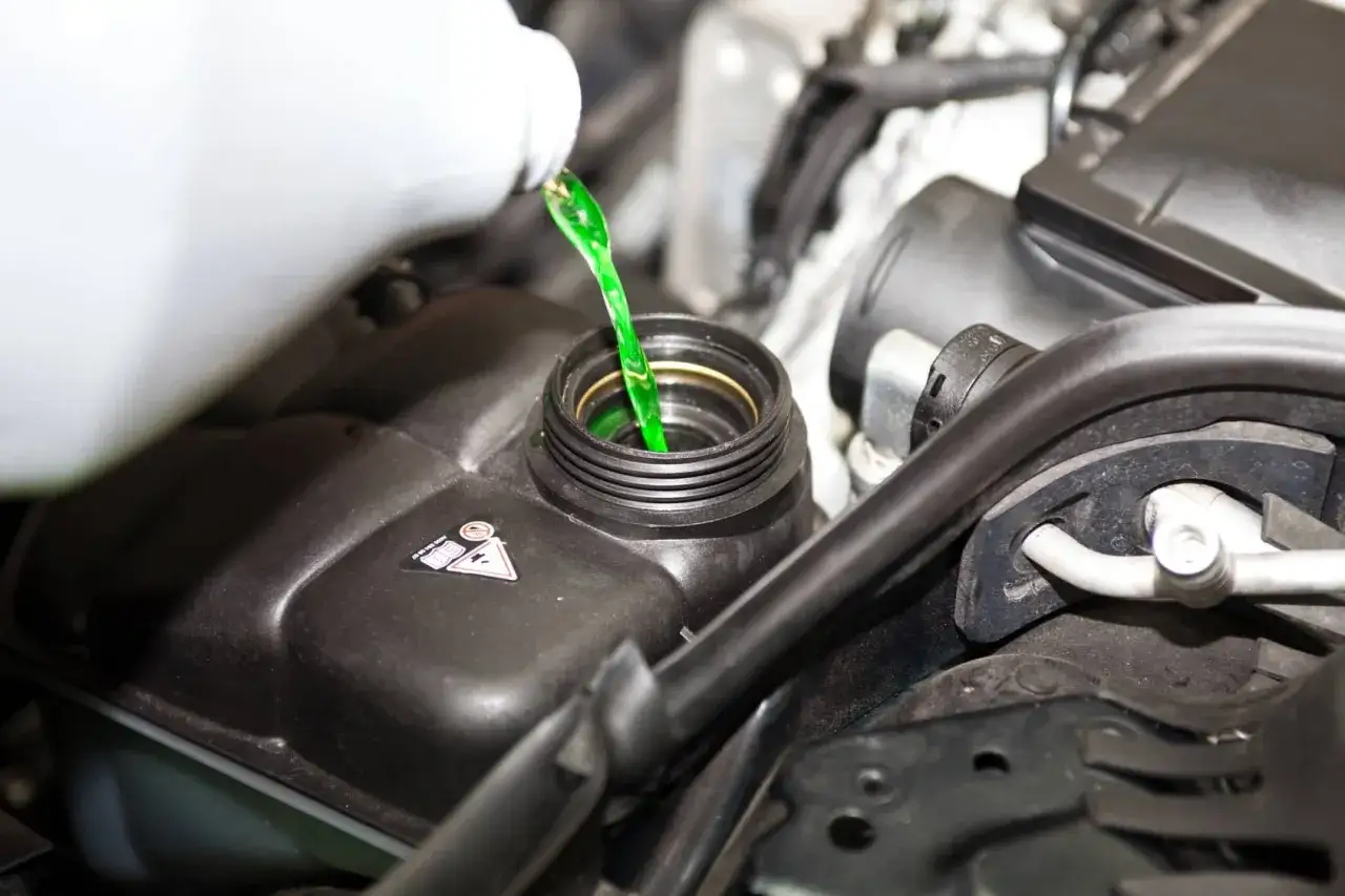 Vertiendo líquido refrigerante verde en el depósito del coche. Un paso esencial para saber como cambiar el liquido refrigerante y mantener tu motor en óptimas condiciones.