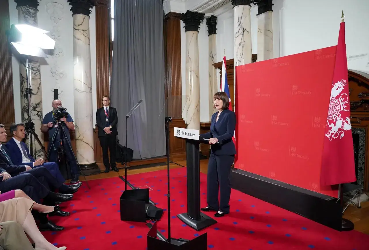A woman speaks at a podium, advocating for personal advocacy in front of a red HM Treasury backdrop.