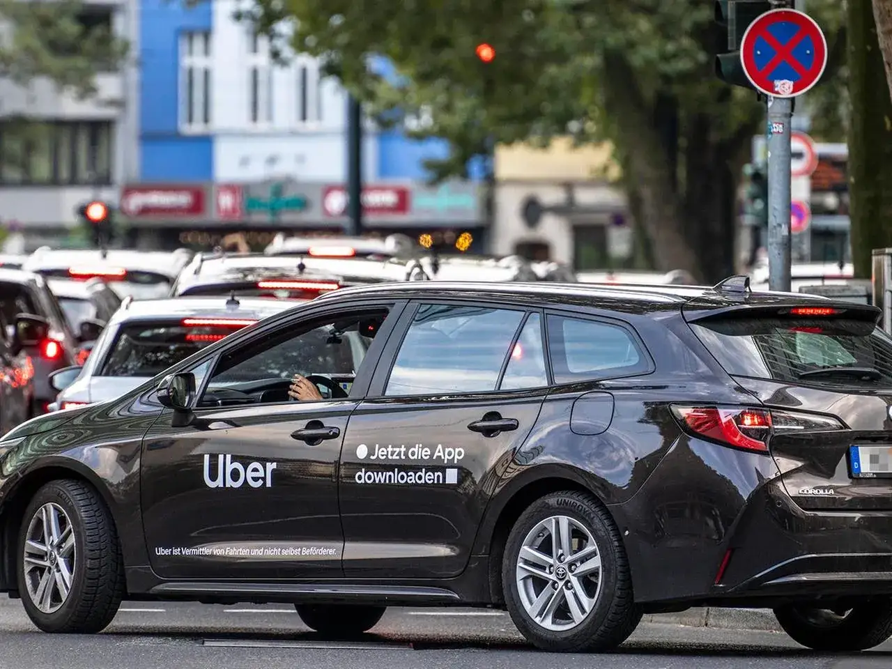 Ein dunkler Kombi mit Uber-Logo steht im Stau. Ein Fahrer hält das Lenkrad. Die App