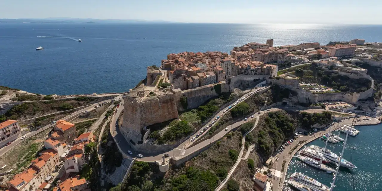 Vue aérienne de Bonifacio, Corse. La citadelle domine la mer bleue, rappelant Ajaccio. Des yachts mouillent dans le port.