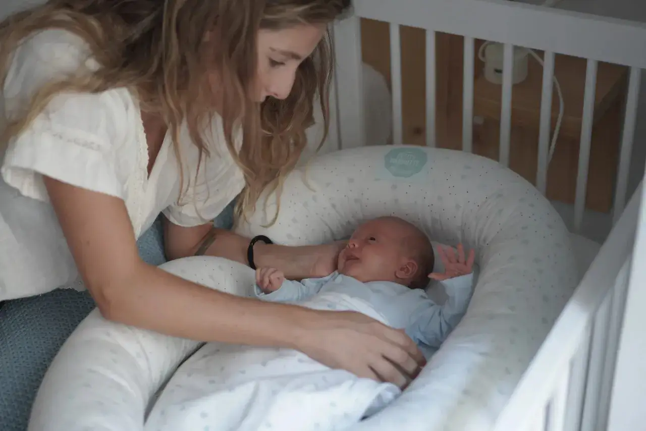 Madre observa a su beb&eacute; reci&eacute;n nacido, listo para sus siestas. El peque&ntilde;o sonr&iacute;e en su nido acogedor.