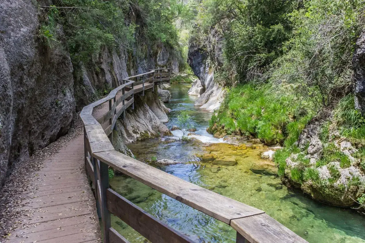 Pasarela de madera junto a río cristalino en cañón, ideal para las mejores rutas senderismo España.