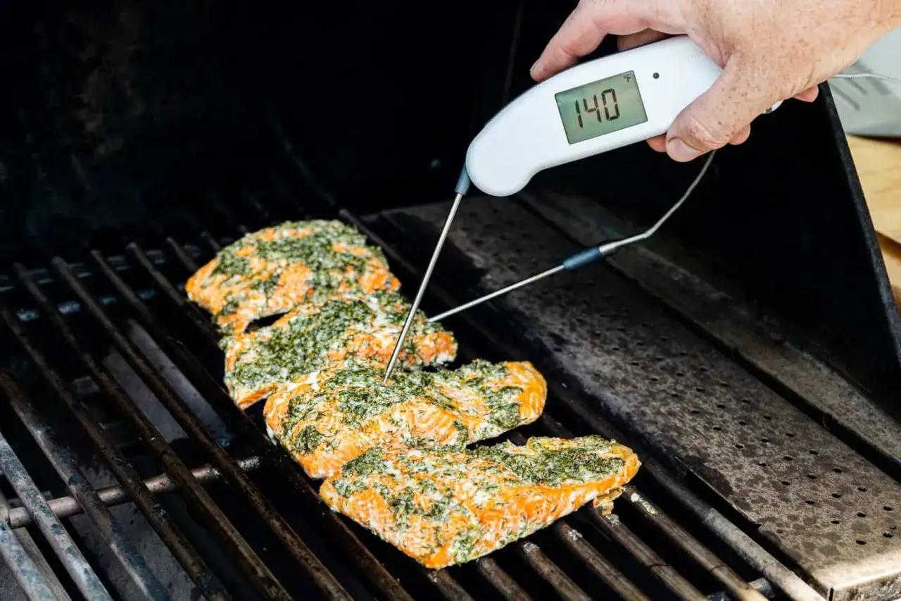 Grillad lax med &ouml;rtkryddor p&aring; grillen, en termometer visar 140&deg;F. Perfekt grillad lax temperatur.