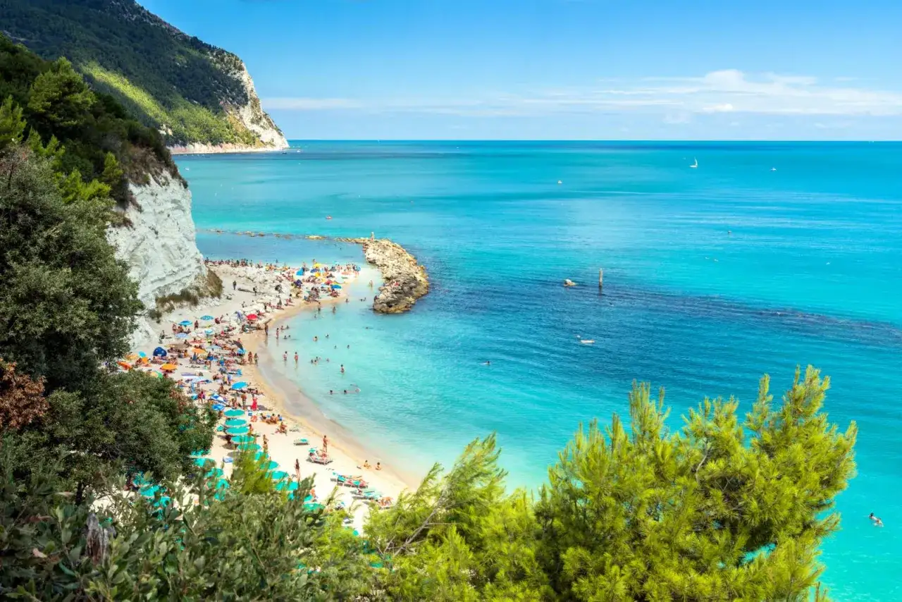 Spiaggia affollata con ombrelloni colorati e gente che nuota nel mare cristallino. In Abruzzo c'&egrave; il mare, una meraviglia azzurra sotto un cielo limpido.