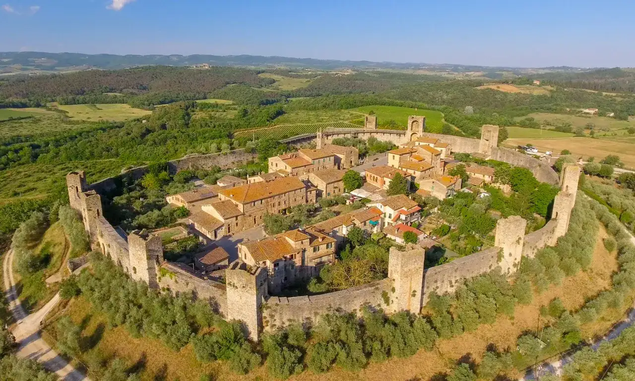 Borgo medievale di San Gusm&egrave;, con mura fortificate e torri, immerso nel paesaggio collinare toscano.