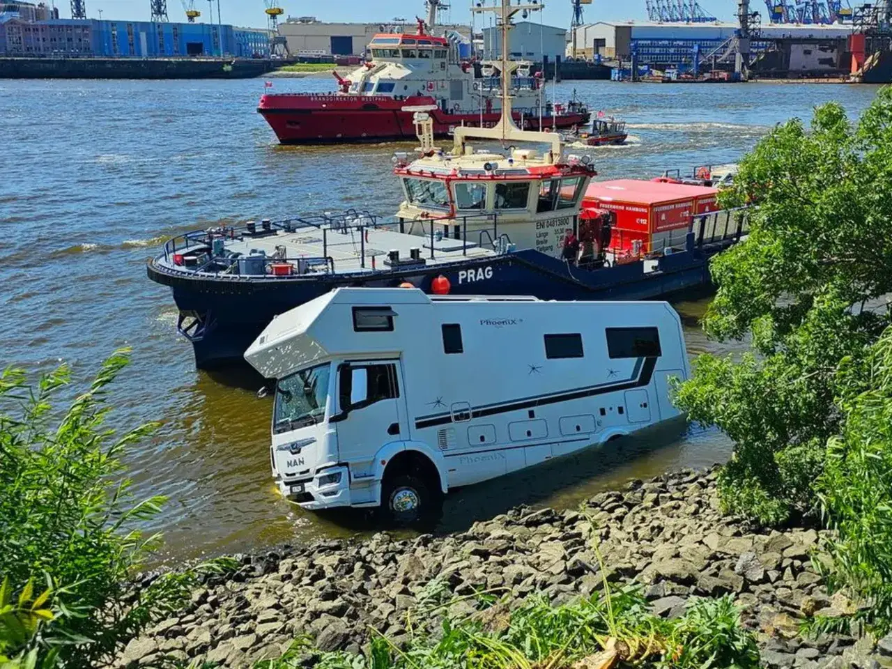 Ein Wohnmobil steckt im Wasser am Ufer des Hamburger Hafens. Ein Schlepper liegt daneben. Ein kurioser Anblick f&uuml;r jeden Hamburg Blog.