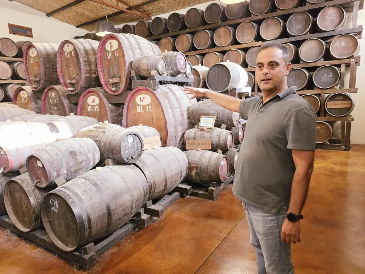 Un uomo indica una cantina piena di botti di legno, alcune etichettate
