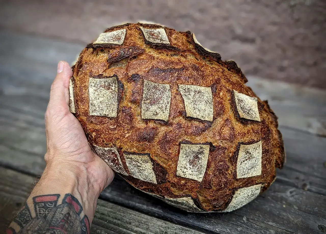 Ein handgehaltener, knuspriger Laib französisches Brot mit einer schönen Kruste und einem Rautenmuster.