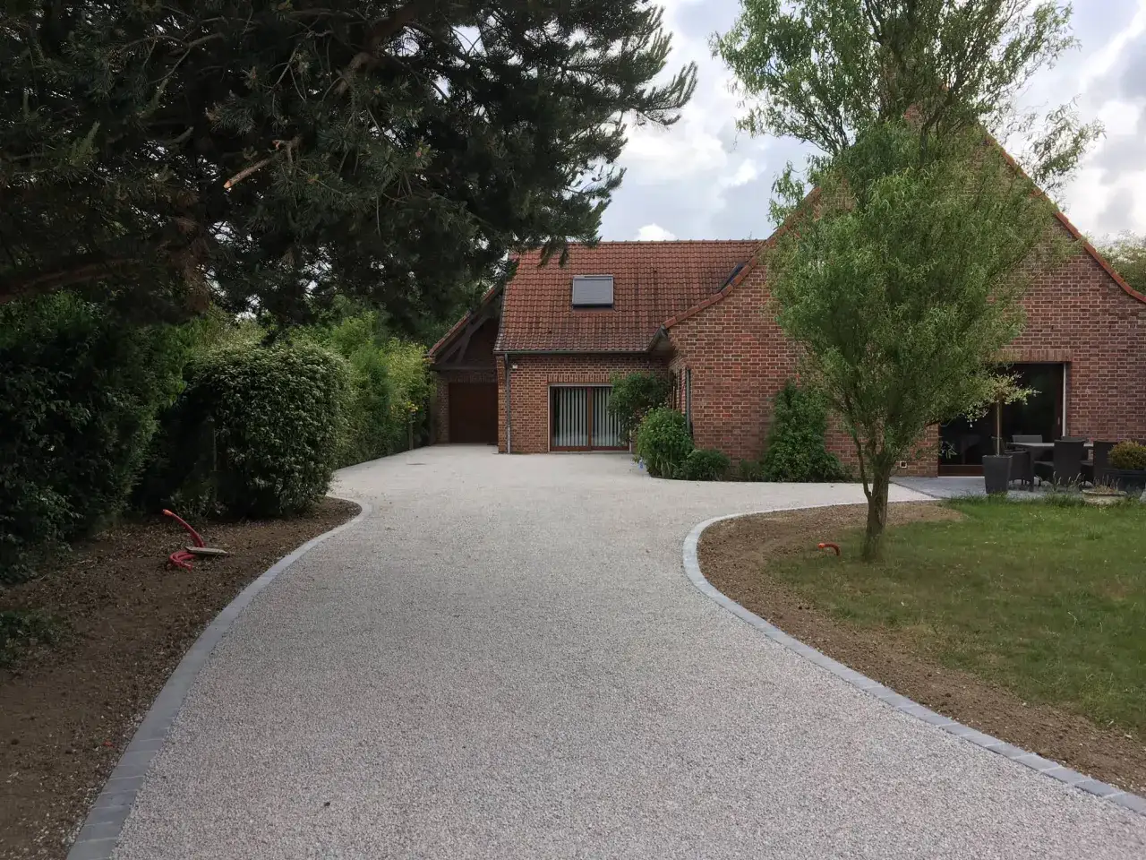 Aménagement paysager pour faire une place de parking dans son jardin. Une allée en gravier mène à une maison en briques.