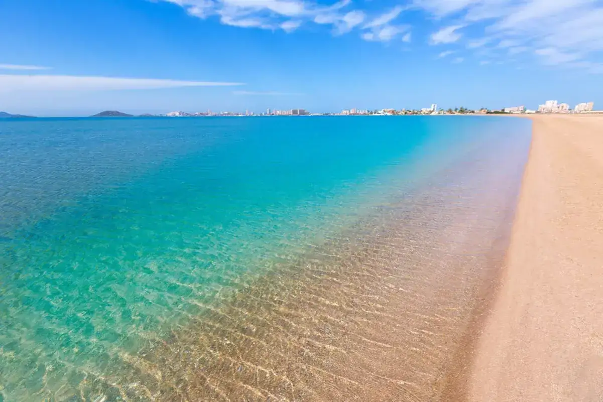 Traumhafter Strand an der Costa C&aacute;lida, Spanien. T&uuml;rkisfarbenes Wasser trifft auf goldenen Sand, im Hintergrund eine Stadtkulisse.