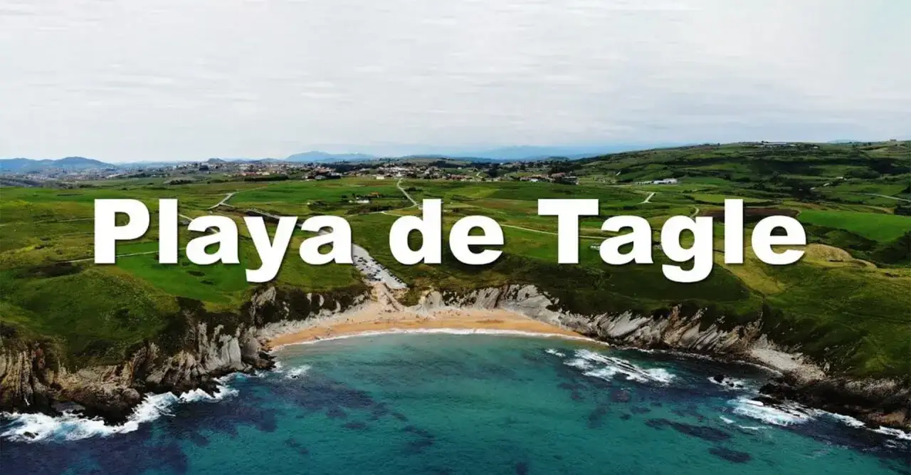 Vista aérea de la **playa de Tagle**, con acantilados verdes, arena dorada y mar turquesa.