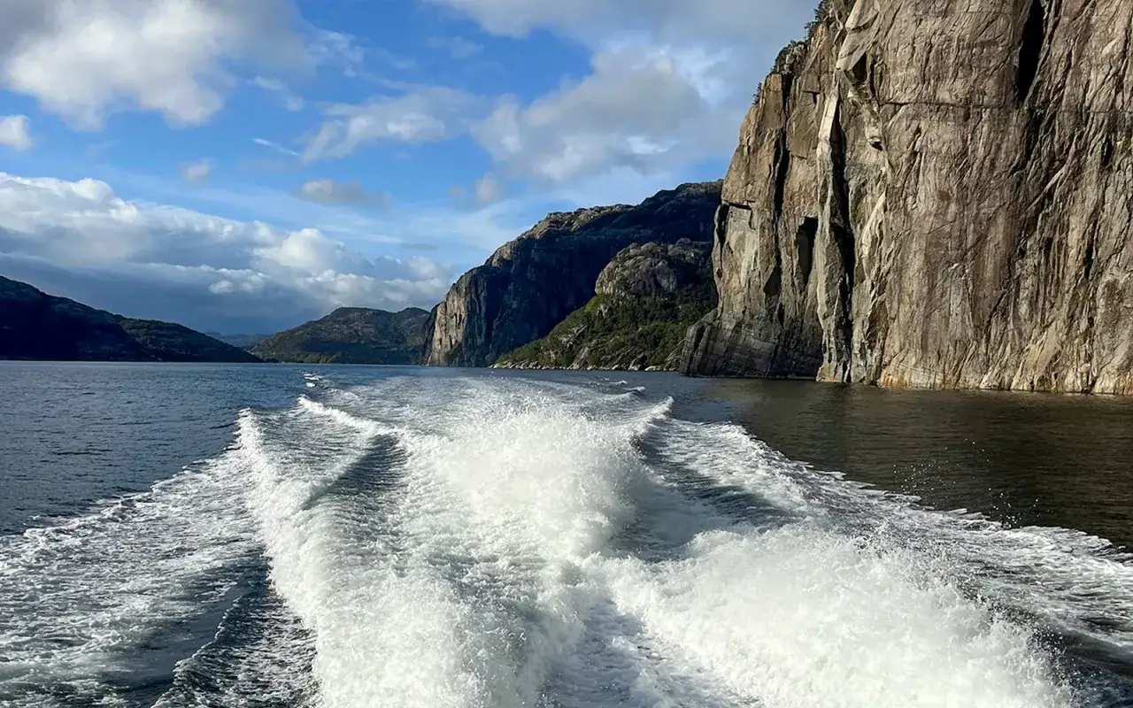 Rejs po majestatycznych **Stavanger fiordy**. Woda pieni się za łodzią, a strome, skaliste zbocza górskie wznoszą się po prawej stronie.