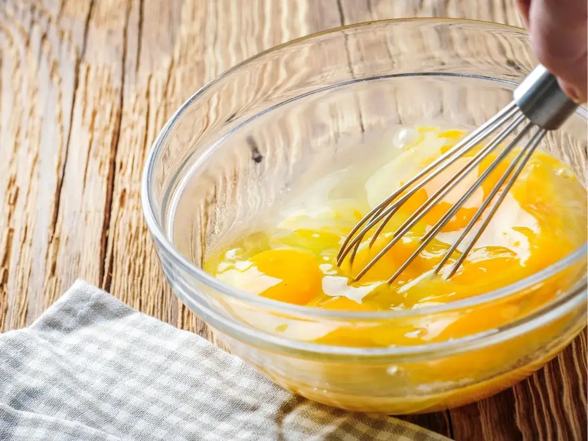 Uova intere in una ciotola di vetro vengono sbattute con una frusta, un passo fondamentale per pastorizzare le uova in modo sicuro per le preparazioni.