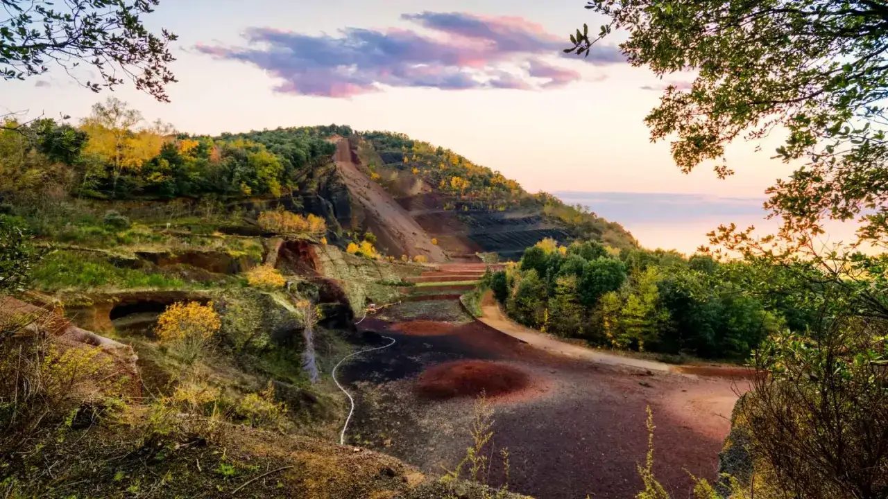Paisaje otoñal en la ruta volcanes Olot. Terrenos volcánicos con vegetación y cielo rosado.