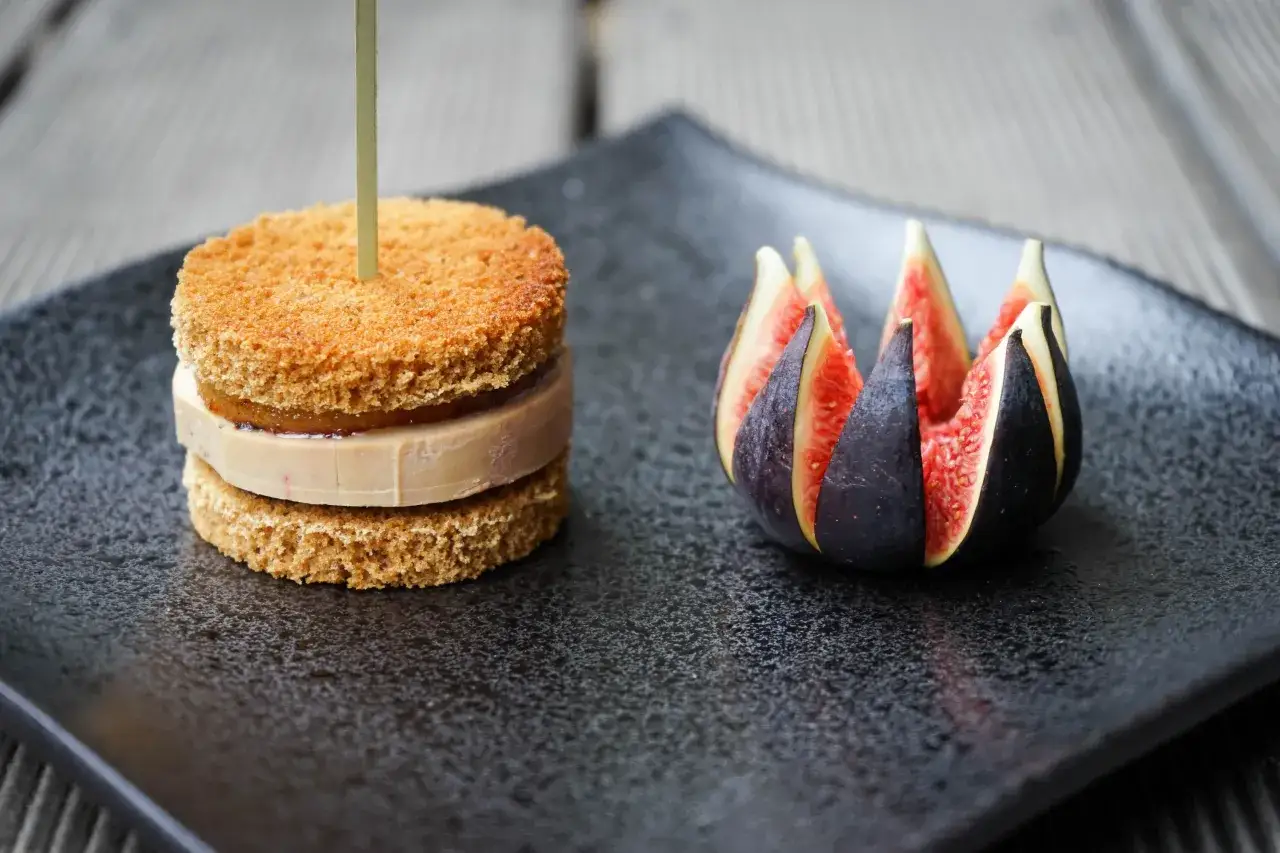Mini burger au foie gras sur pain brioch&eacute;, accompagn&eacute; de figues coup&eacute;es en quartiers sur une assiette noire.