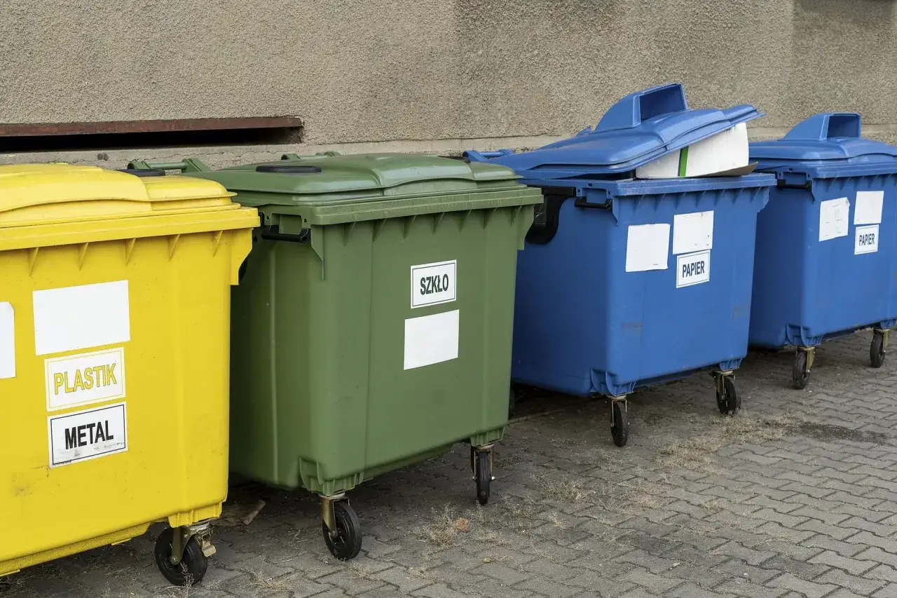 Rzędy kolorowych śmietników: żółty (plastik, metal), zielony (szkło) i niebieskie (papier). Idealne do planowania, jak mierzyć odległość śmietnika od okien.