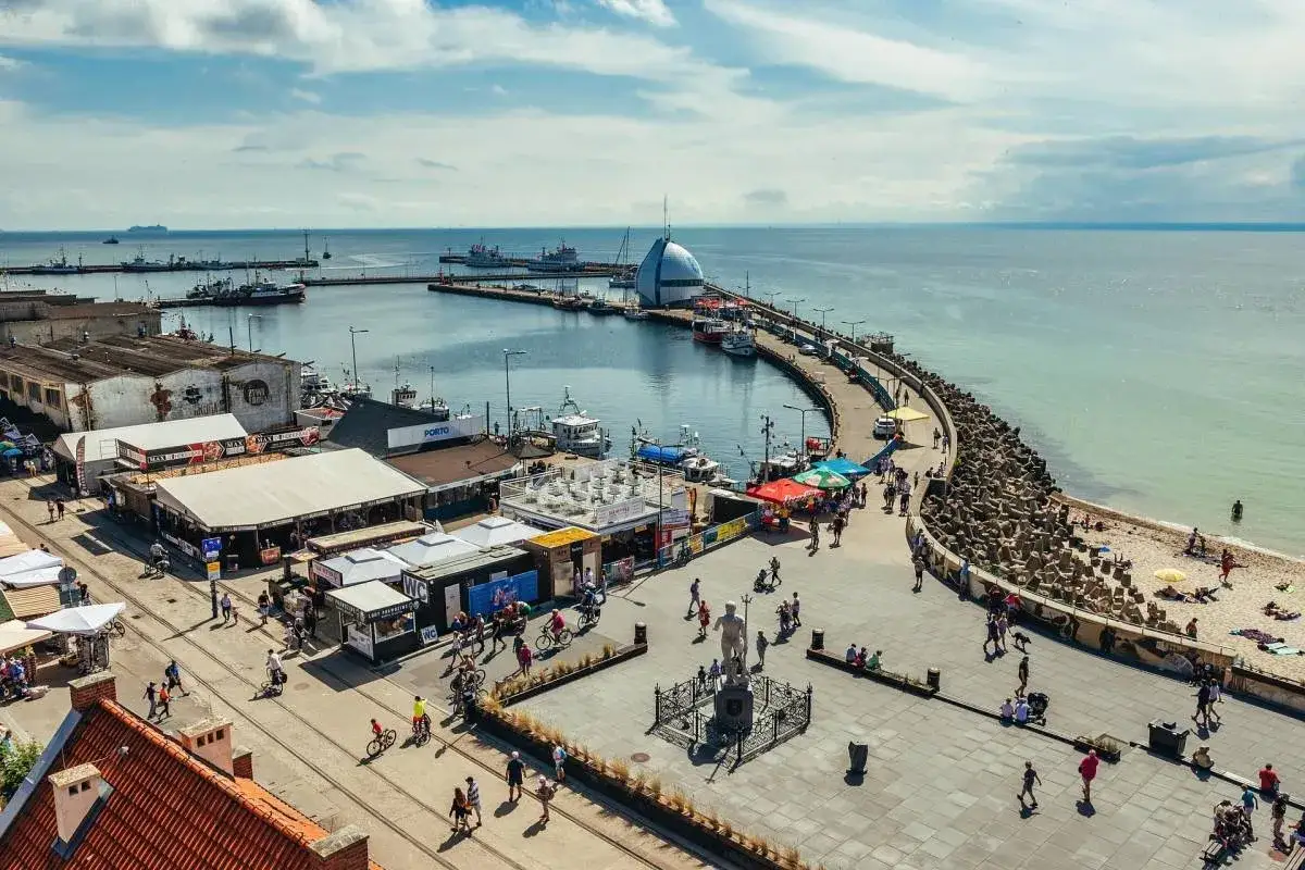 Tętniące życiem hel miasto portowe z łodziami, ludźmi spacerującymi po promenadzie i plażą.