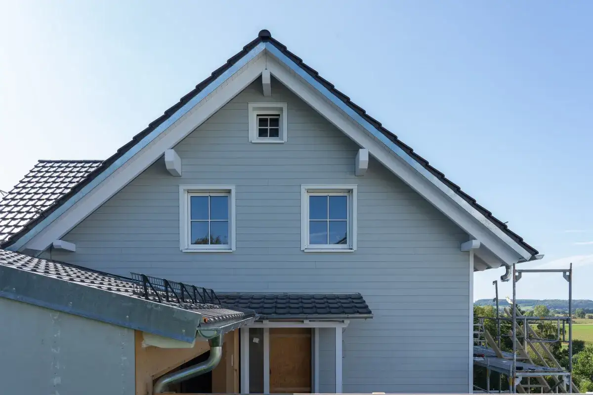 Fassadenverkleidung aus Faserzement an einem Haus mit Fenstern und Dach.